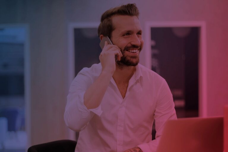 lächelnder Mann am Laptop und mit Mobiltelefon am Ohr