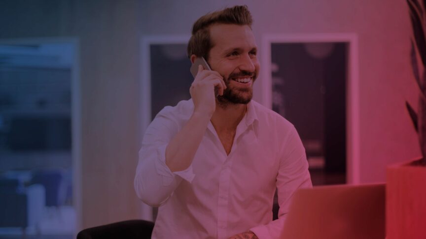 lächelnder Mann am Laptop und mit Mobiltelefon am Ohr